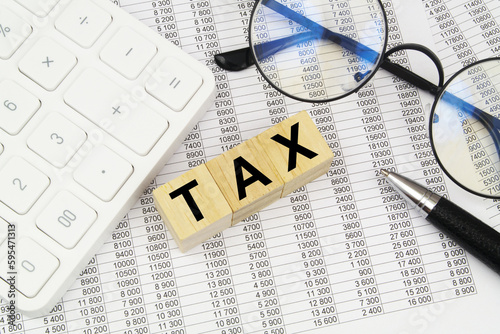 Word tax on wooden cubes, calculator, pen and eyeglasses on financial documents.