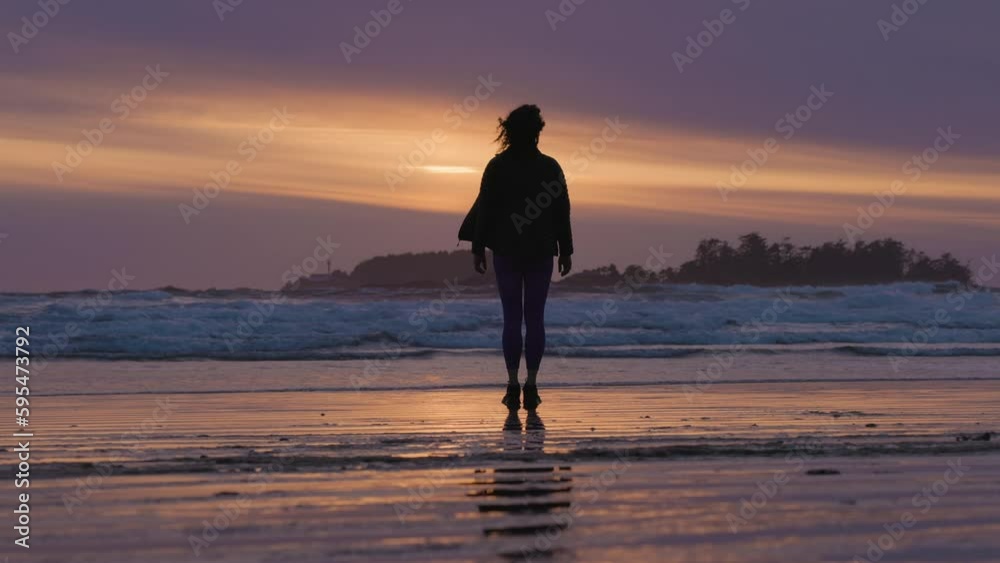Adventurous Woman Standing on the Sandy Beach on the West Coast of Pacific Ocean. Cox Bay in Tofino, Vancouver Island, BC, Canada. Adventure Travel. Slow Motion Adventurous Woman Standing on the Sandy Beach on the West Coast of Pacific Ocean. Cox Bay in Tofino, Vancouver Island, BC, Canada. Adventure Travel. Slow Motion