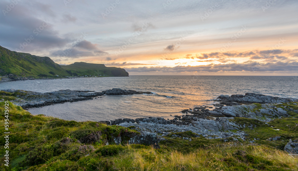 Wonderful sunset above the sea  on Runde island with fresh grass in the foreground and mountains in the background. Runde, Møre og Romsdal, Norway