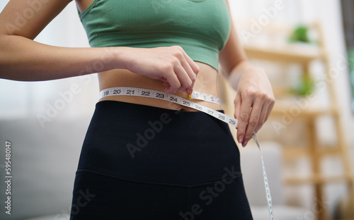 Asian healthy woman dieting Weight loss. Slim woman measuring waist with measure tape after diet at home weight control.