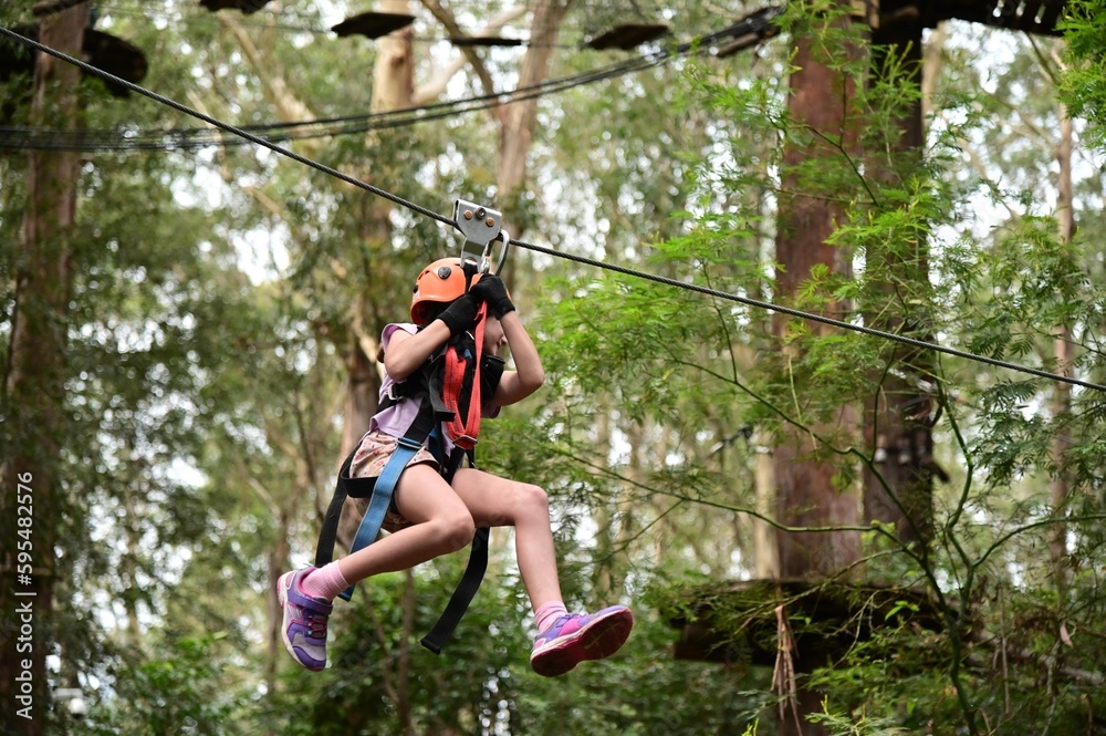 Young girl sliding on a flying fox zip line during a treetop adventure climbing