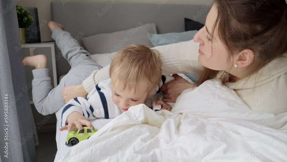 Portrait of smiling toddler boy with young mother lying in bed and hugging. Concept of family happiness, relaxing at home, having fun in bed, parent and cheerful kids. Portrait of smiling toddler boy with young mother lying in bed and hugging. Concept of family happiness, relaxing at home, having fun in bed, parent and cheerful kids.