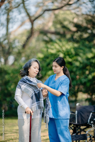 Asian young caregiver nurse support senior older male walking outdoors. Specialis doctor help and take care of elderly mature. Nursing home hospital garden