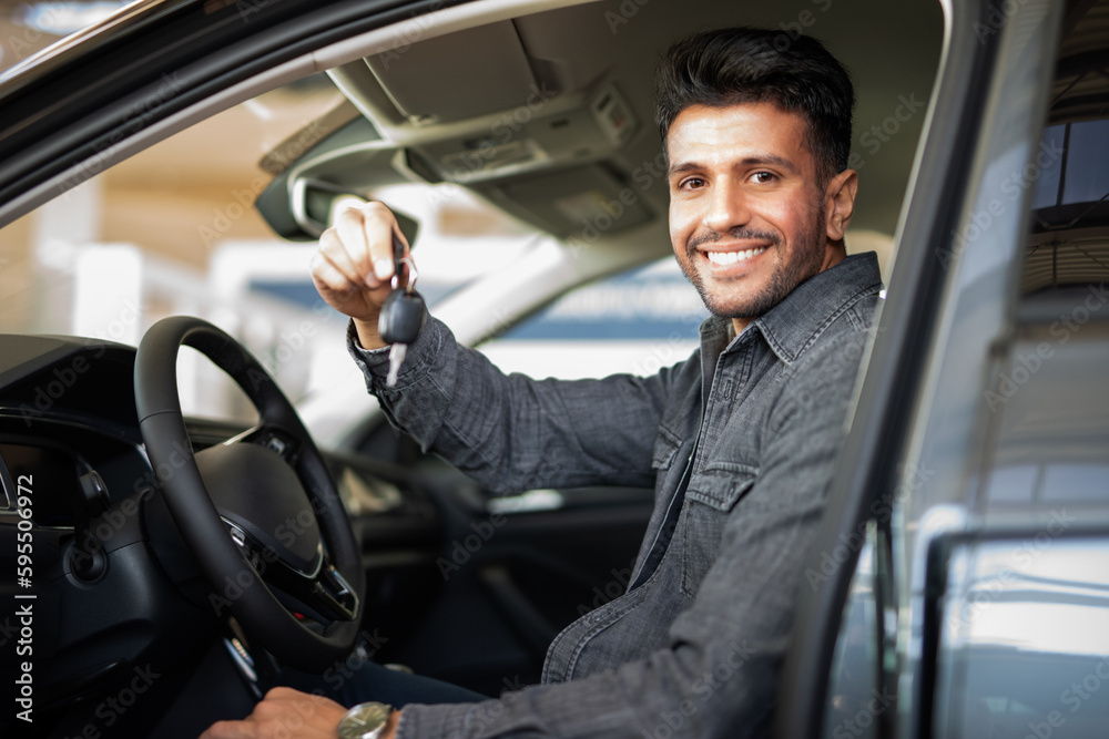 Man showing the key of his new car in a car dealer saloon Man showing the key of his new car in a car dealer saloon
