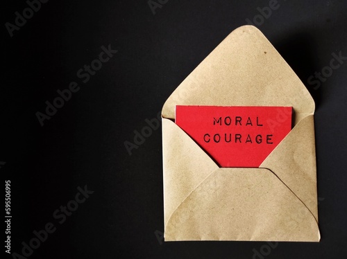 Craft envelope on black background with text on red card MORAL COURAGE, means courage to take action for moral reasons or act upon ethical values to help others during difficult ethical dilemmas
