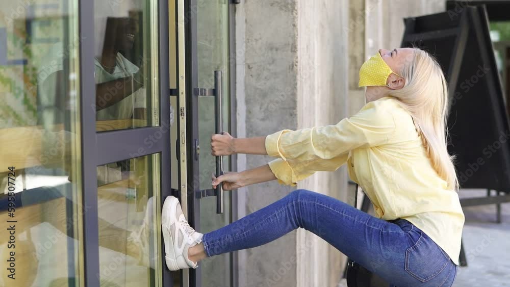 An impatient Caucasian woman opens the door of the store with her foot, a young blonde in a medical mask really wants to get into the store.