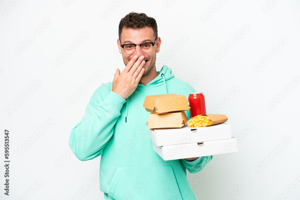 Young caucasian man holding fast food isolated on white background happy and smiling covering mouth with hand Young caucasian man holding fast food isolated on white background happy and smiling covering mouth with hand