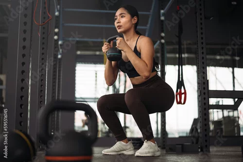 Panel kuchenny z motywem Strong asian woman doing exercise with kettlebell at crossfit gym. Athlete female wearing sportswear workout on grey gym background with weight and dumbbell equipment. Healthy lifestyle.