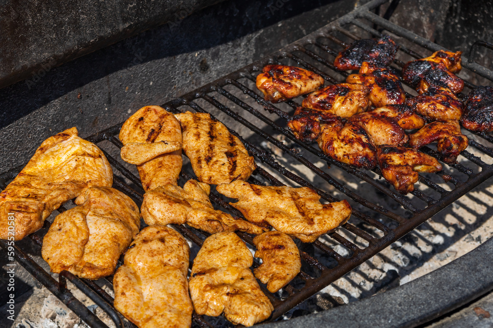 Chicken breasts and chicken wings are marinated and grilled on an outdoor grill.
