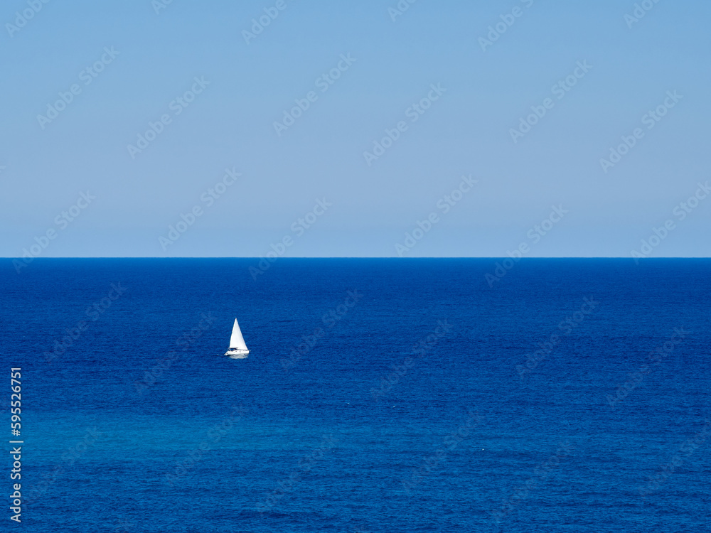 White sailboat in the Mediterranean sea in Costa Blanca. Altea, province of Alicante, Comunidad de Valencia, Spain. Nautical blue background with copy space