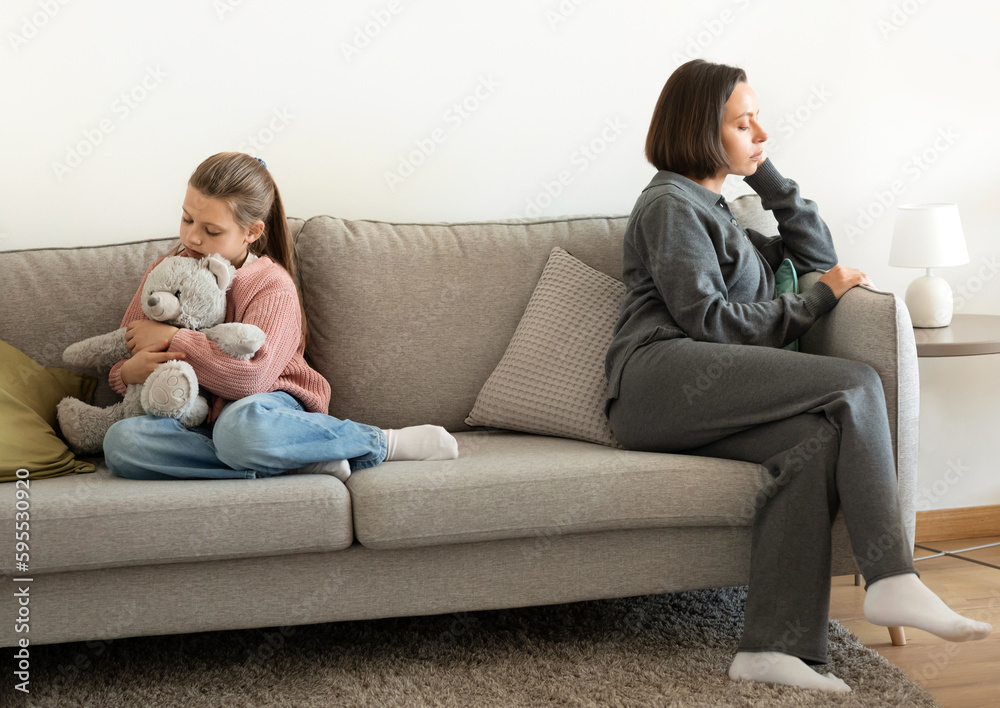 Sad offended european millennial mom ignores teen girl, sit on sofa in living room interior after quarrel