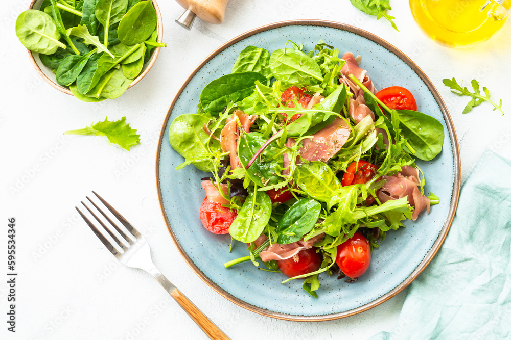 Green salad with fresh leaves, tomatoes and jamon at white table. Top view with copy space. Green salad with fresh leaves, tomatoes and jamon at white table. Top view with copy space.