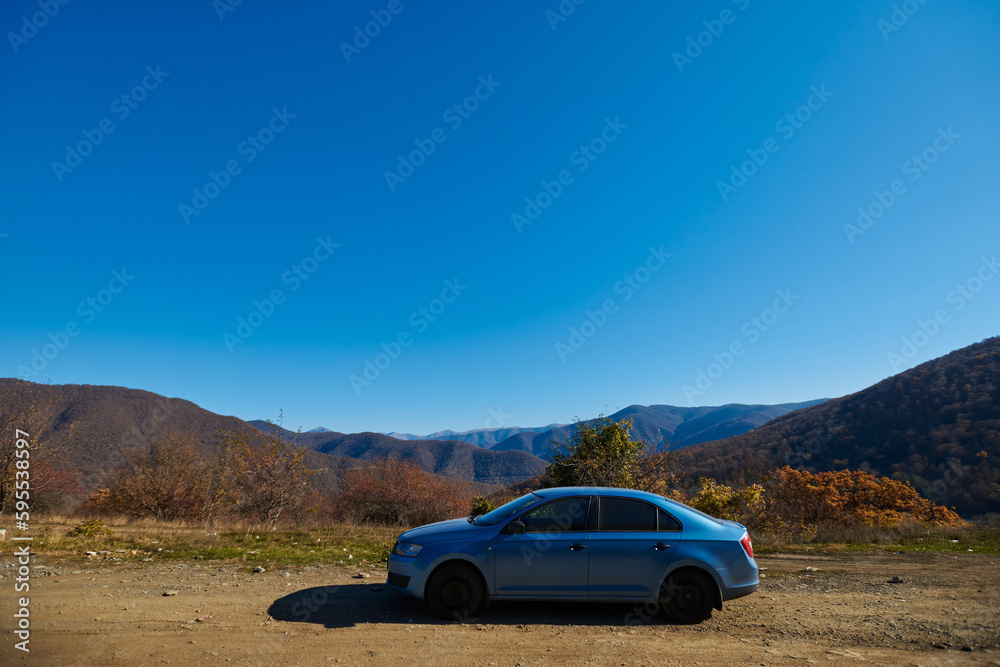 beautiful mountain autumn landscape. a blue car is parked on the side of the road. travel by car. beautiful mountain autumn landscape. a blue car is parked on the side of the road. travel by car.