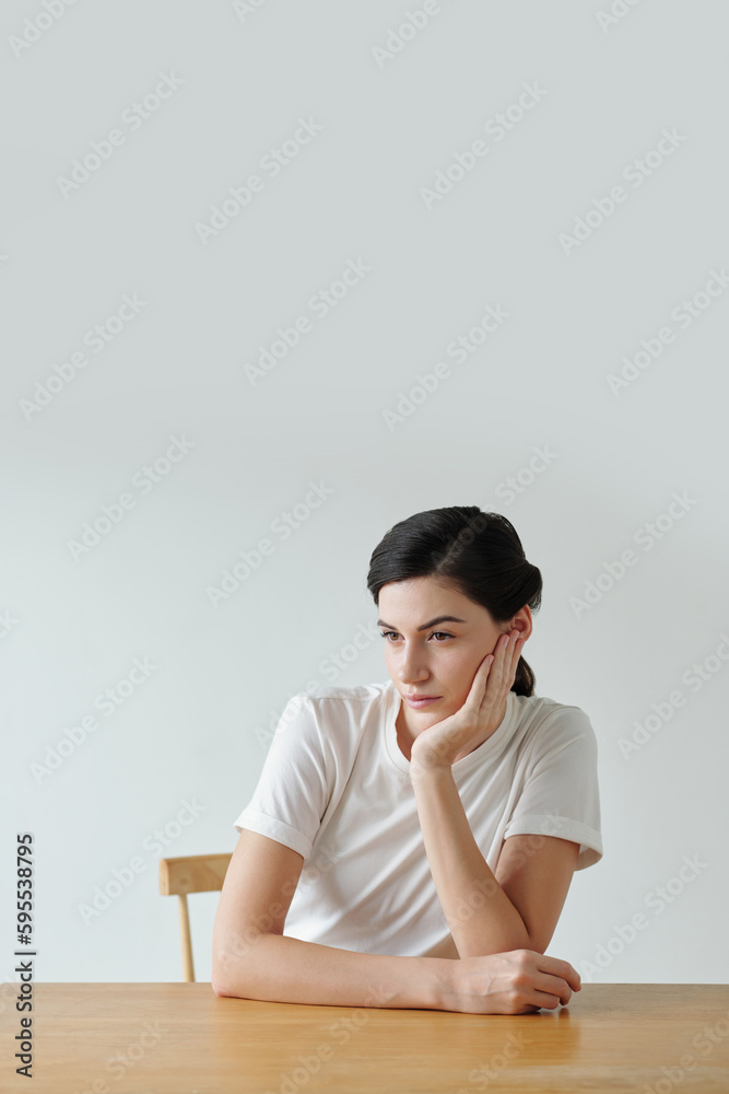 Portrait of pensive young woman sitting at table and looking away Portrait of pensive young woman sitting at table and looking away