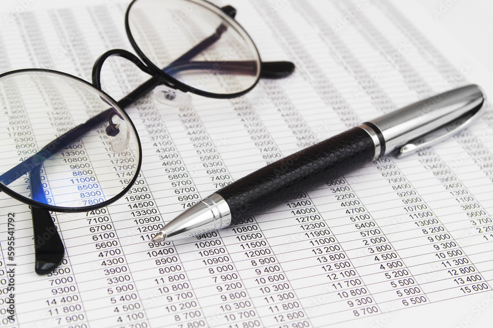 Round black eyeglasses and metallic pen on financial reports papers. Business concept. Round black eyeglasses and metallic pen on financial reports papers. Business concept.