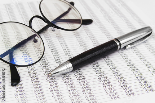 Round black eyeglasses and metallic pen on financial reports papers. Business concept. 