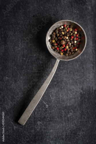 Big old spoon with peppercorn on black background
