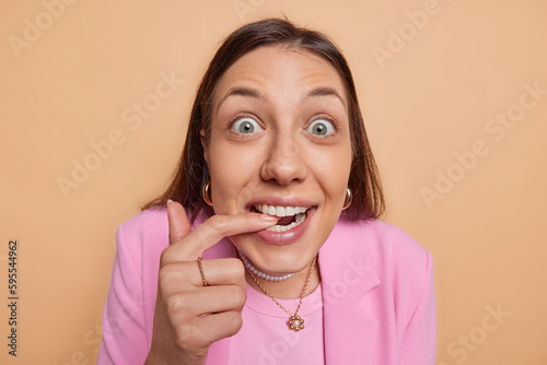 Fényképezés Close up shot of beautiful dark haired woman bites finger and stares at camera w