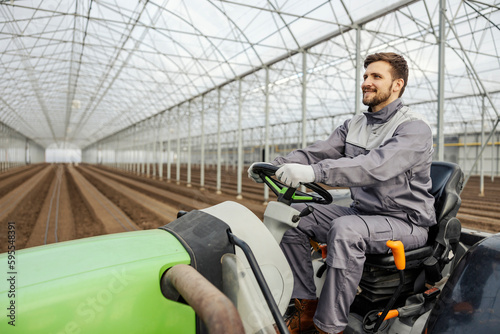 A happy agronomist is cultivating the land in hothouse while driving tractor. photo