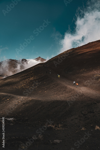 Tourists walk on mountain paths of Etna volcano. Groups of hikers explore and photograph the view from the top of big craters. Mountain life, extreme sports, geological wonders and lunar landscapes. © Pier Fax