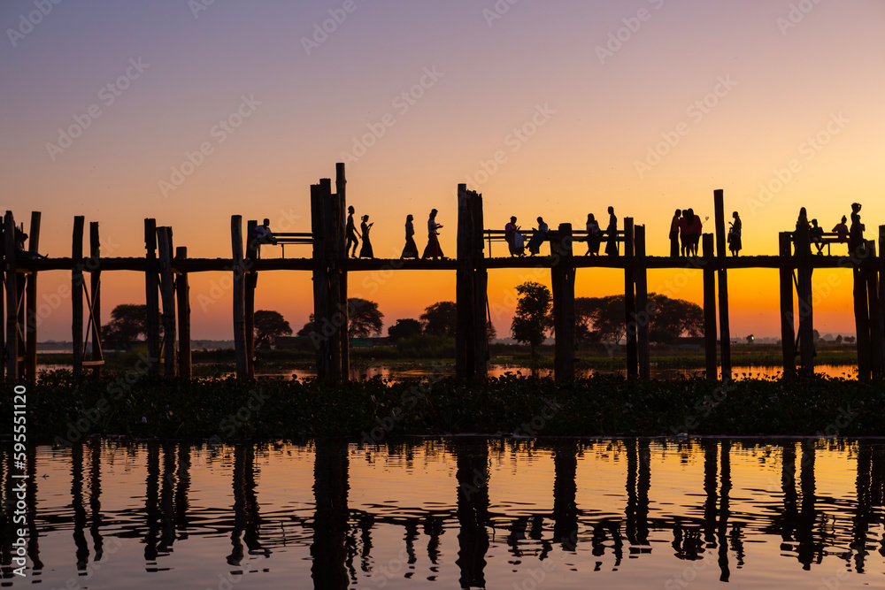 Unidentified people walk on U Bein bridge at sunset in Myanmar. U Bein bridge is the longest teak bridge in the world, Amarapura, Myanmar