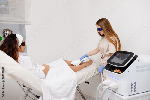 Beautician making hair removing procedure on legs for woman client. Laser epilation and cosmetology in beauty salon