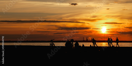Panoramic view of silhouettes people walking by urban seaside at amazing city sunset background. Panorama of evening urban landscape for ad banner. Vitality and city life concept. Copy text space