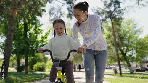 happy child learns to ride a two-wheeled bicycle in the park. Mom teaches her daughter how to ride a bike. sport life. walk outdoors in the park. concept children dream bike. mother and kid daughter © Валерий Зотьев