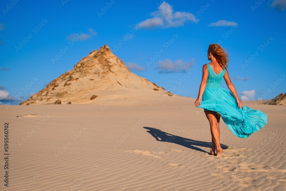 Beautiful blonde woman on hot sand with blue sky in the background. Photo taken on the shifting dunes over the Baltic Sea in Leba, Poland. Photo with a shallow depth of field with blurred background. Beautiful blonde woman on hot sand with blue sky in the background. Photo taken on the shifting dunes over the Baltic Sea in Leba, Poland. Photo with a shallow depth of field with blurred background.