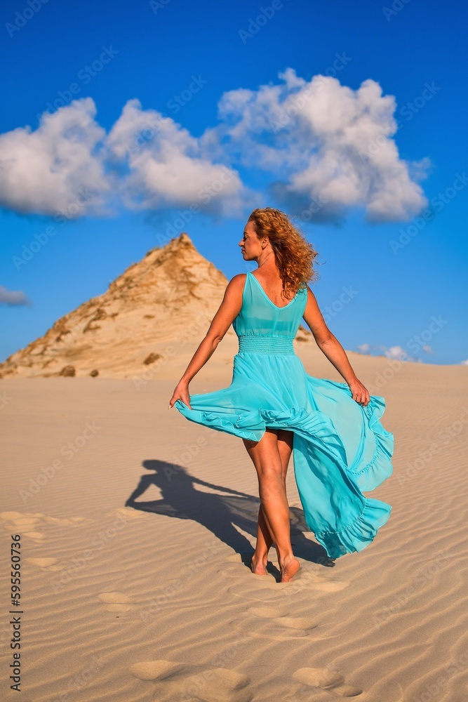 Beautiful blonde woman on hot sand with blue sky in the background. Photo taken on the shifting dunes over the Baltic Sea in Leba, Poland. Photo with a shallow depth of field with blurred background. Beautiful blonde woman on hot sand with blue sky in the background. Photo taken on the shifting dunes over the Baltic Sea in Leba, Poland. Photo with a shallow depth of field with blurred background.