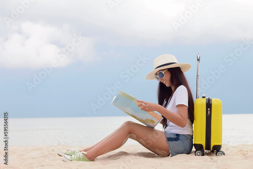 Summer Party. Traveler and tourism woman travel in summer on the beach and white sand. Asian is reading a map with yellow suitcase. On working in vacation concept