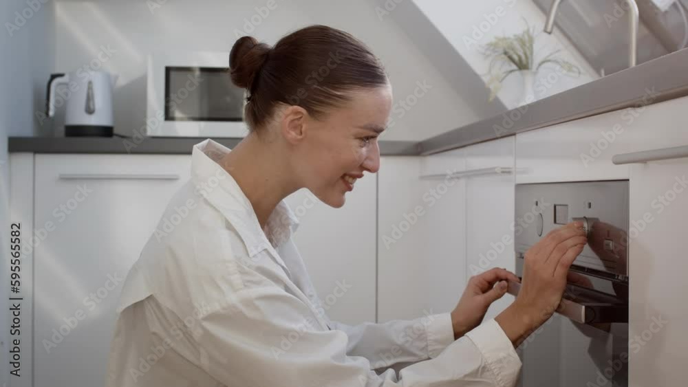 Modern domestic technologies. Young happy lady turning on baking mode on oven and checking pastry condition, empty space Modern domestic technologies. Young happy lady turning on baking mode on oven and checking pastry condition, empty space