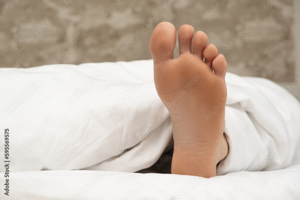 Male legs stick out from under the blanket, sweet sleep in a comfortable bed