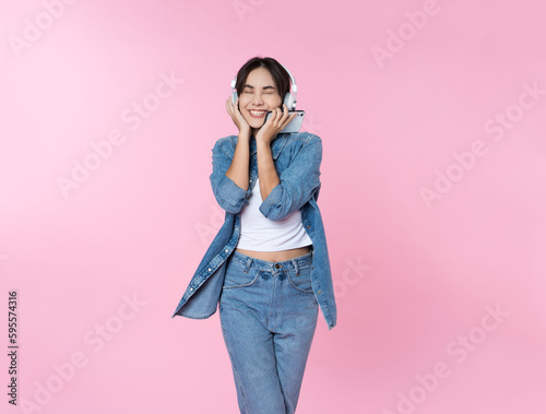 Young Asian woman wearing headphones dancing and listening to music from smartphone shoot in isolated on pink background