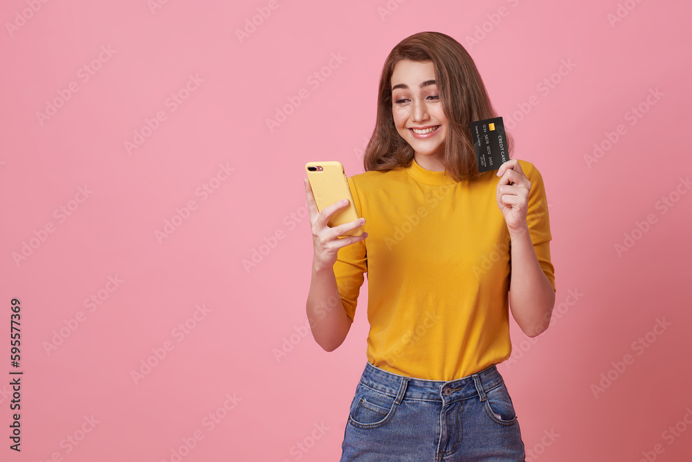 happy smiling young woman using mobile phone with credit card for shopping and payment online isolated on pink studio background. happy smiling young woman using mobile phone with credit card for shopping and payment online isolated on pink studio background.