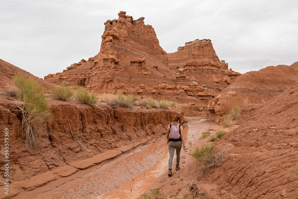 Woman walking along temporary mud river flowing down Goblin Valley State Park, Utah, USA. Scenic canyon hiking trail with unique eroded sandstone hoodoo rock formations called goblins on cloudy day Woman walking along temporary mud river flowing down Goblin Valley State Park, Utah, USA. Scenic canyon hiking trail with unique eroded sandstone hoodoo rock formations called goblins on cloudy day