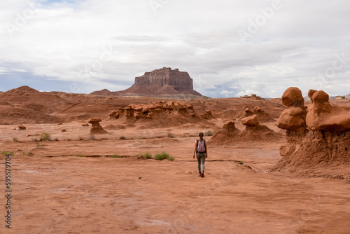 Woman hiking next to unique eroded Hoodoo Rock Formations at Goblin Valley State Park in Utah, USA, America. Scenic view of Entrada sandstone mountain peak Wild Horse Butte in the back. Overcast