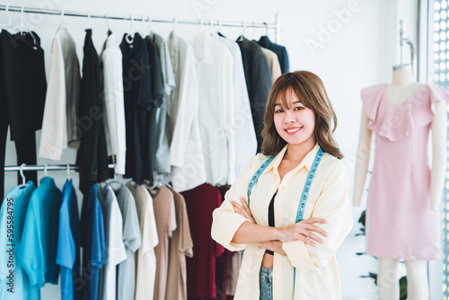 Beautiful designer standing with arms crossed in workshop full of clothes and mannequins.