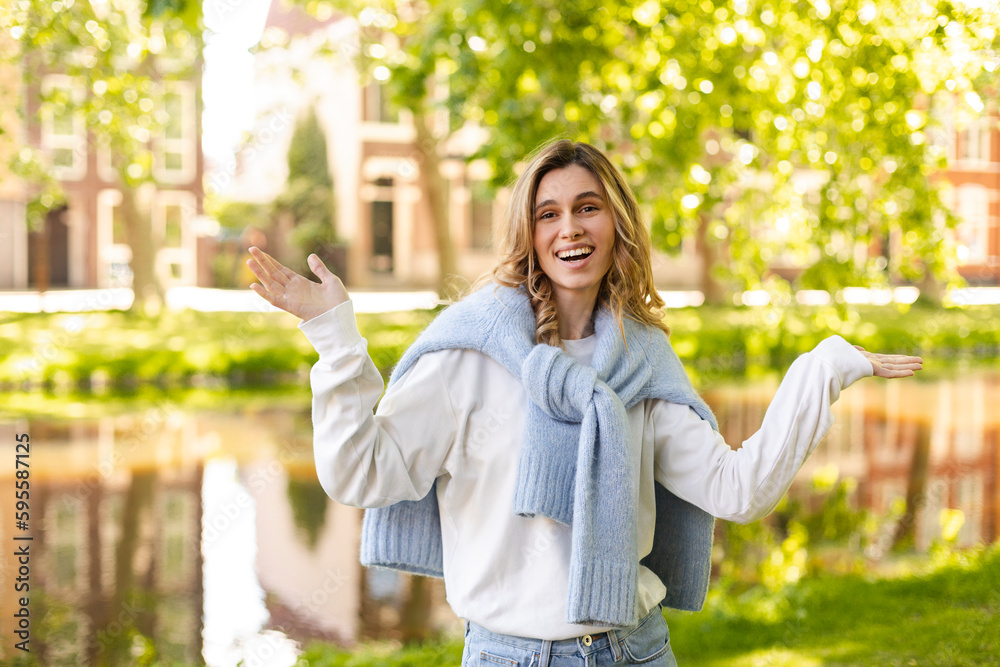 Beautiful woman smiling and look at camera at park at sunny day. Outdoor portrait of a smiling curly blonde girl. Happy cheerful girl laughing at park, spread her hands and show toothy smile. Beautiful woman smiling and look at camera at park at sunny day. Outdoor portrait of a smiling curly blonde girl. Happy cheerful girl laughing at park, spread her hands and show toothy smile.