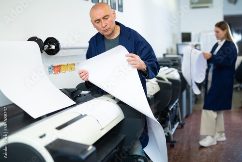 Service man uses plotter and checks the functionality in printing shop