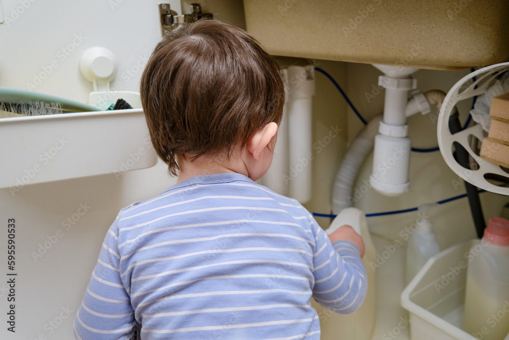 A child is playing with chemical cleaning products under the sink in the kitchen. Baby holds bottles with detergent. Kid aged about two years (one year nine months) A child is playing with chemical cleaning products under the sink in the kitchen. Baby holds bottles with detergent. Kid aged about two years (one year nine months)