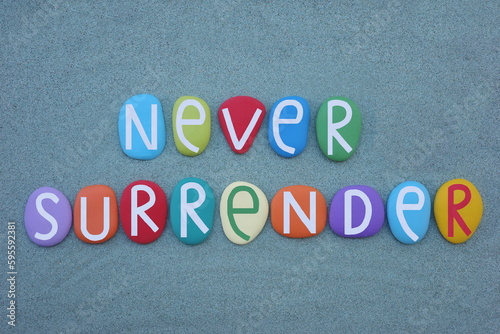 Never surrender, motivational message composed with multi colored stone letters over green sand