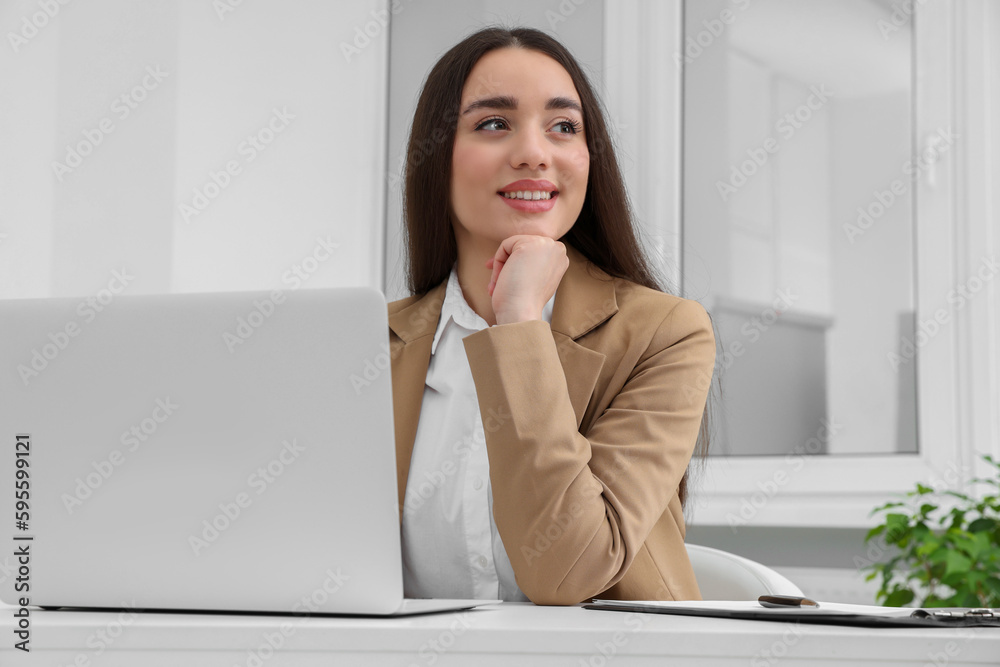 Young female intern working with laptop at table in office Young female intern working with laptop at table in office