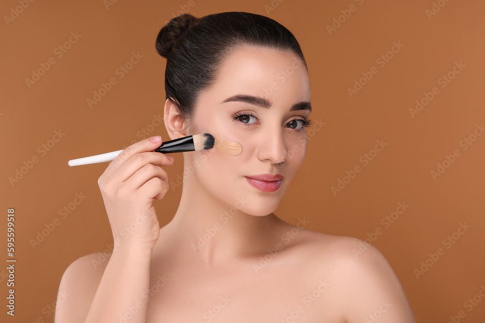 Fototapeta premium Woman applying foundation on face with brush against brown background