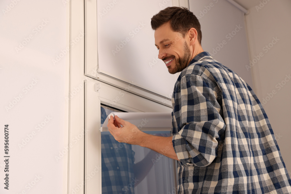 Man installing modern roller window blind indoors Man installing modern roller window blind indoors