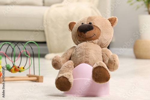 Cute teddy bear on pink baby potty in room. Toilet training