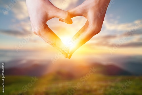 Hand making a heart shape on bokeh background.