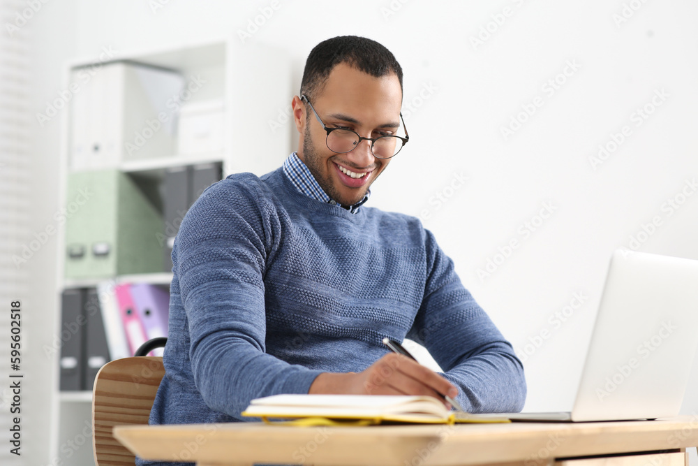 Smiling African American man writing in notebook at wooden table Smiling African American man writing in notebook at wooden table
