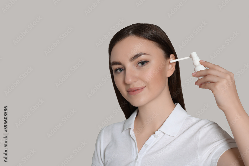Young woman using ear spray on light grey background. Space for text Young woman using ear spray on light grey background. Space for text
