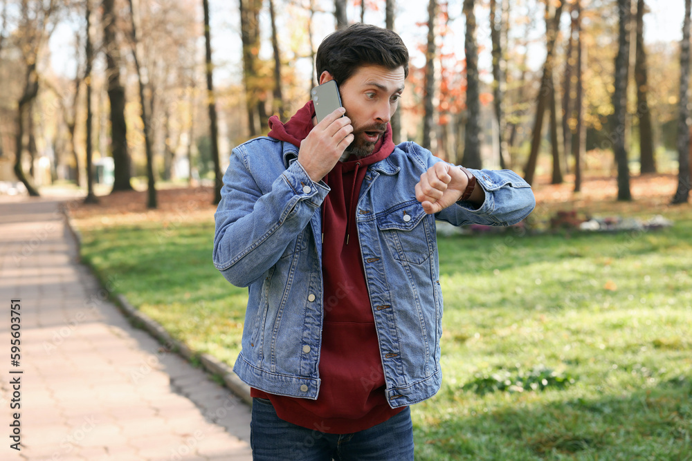 Emotional man talking by smartphone and checking time on watch in park. Being late concept Emotional man talking by smartphone and checking time on watch in park. Being late concept